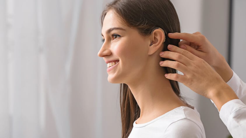 A hearing aid is applied to a woman's ear
