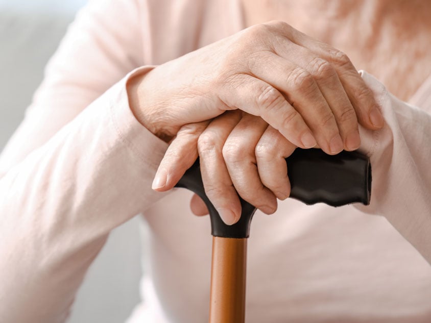 A person puts their hands on a walking stick